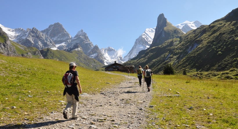 quatre randonneurs s'approchant sur une piste au refuge des barmettes à pralognan en vanoise dans les alpes avec les montagnes du col de la vanoise au fond